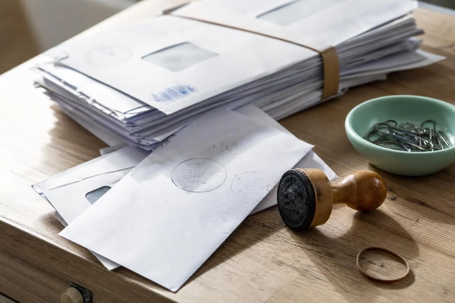 Pile d’enveloppes a fenetre retournees a l’expediteur, maintenues par un elastique a cote d’un tampon en bois